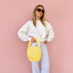 Daffodil yellow handmade crochet Cha Cha Mini bag featuring a crescent-shaped body, braided loop detailing, ruched scrunchie handle and flowing fringe. 