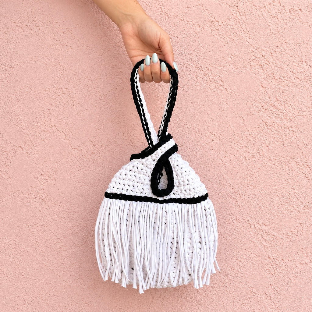 Handmade crochet mini swing bag in Gardenia white with flowing fringe, Onyx black trim and a loop-through wristlet handle.