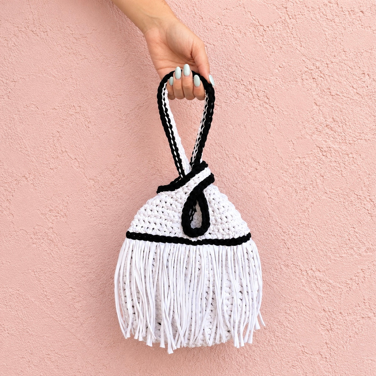 Handmade crochet mini swing bag in Gardenia white with flowing fringe, Onyx black trim and a loop-through wristlet handle.