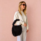 Onyx black handmade crochet Cha Cha Mini bag featuring a crescent-shaped body, braided loop detailing, ruched scrunchie handle and flowing fringe. 