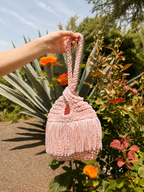 Handmade Petal pink crochet fringe mini swing bag by Daisy C. photographed in a blooming garden.