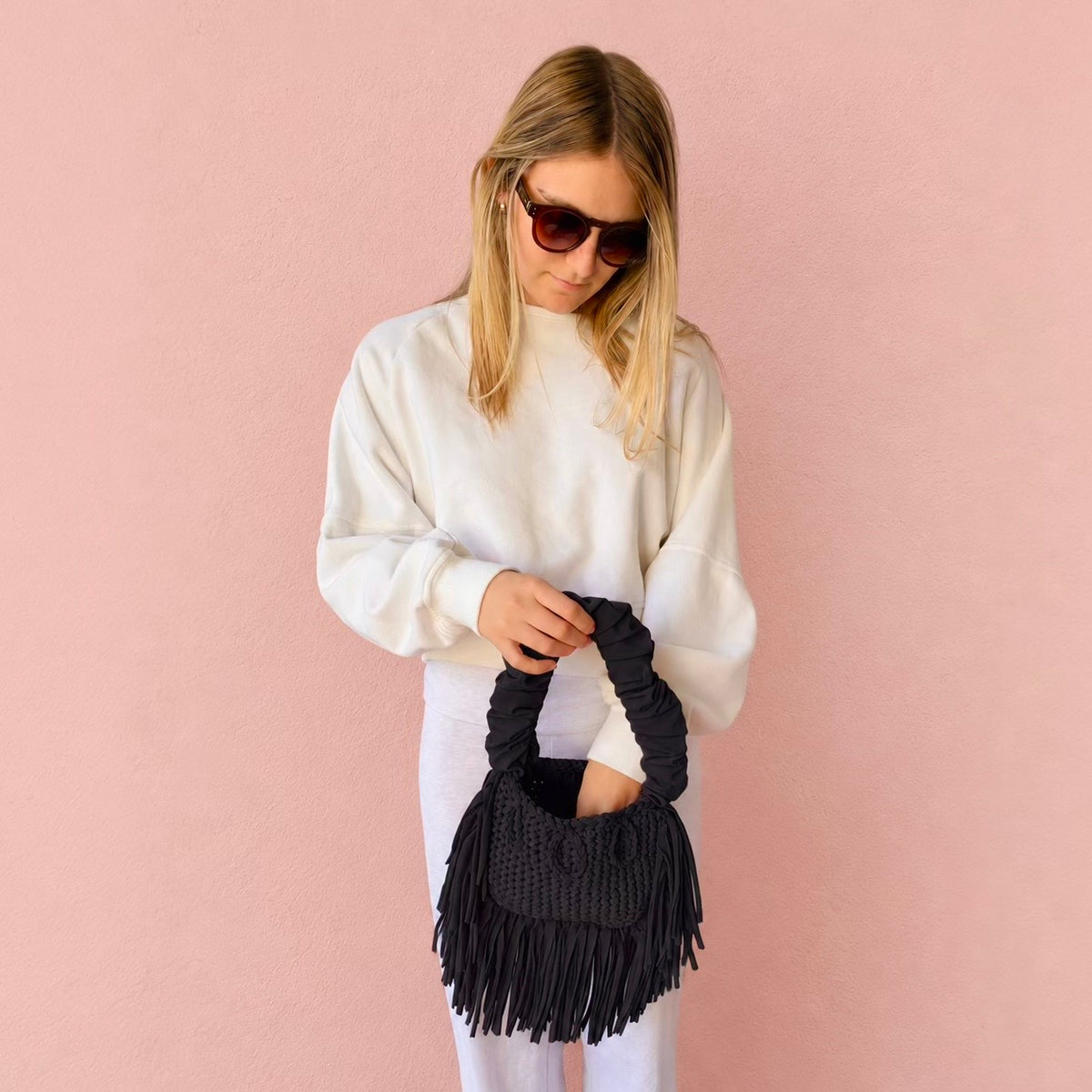 Onyx black handmade crochet Cha Cha Mini bag featuring a crescent-shaped body, braided loop detailing, ruched scrunchie handle and flowing fringe. 
