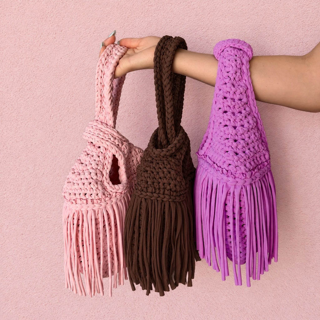 Handmade crochet mini swing bags in light pink, brown and purple with flowing fringe and a loop-through wristlet handle.