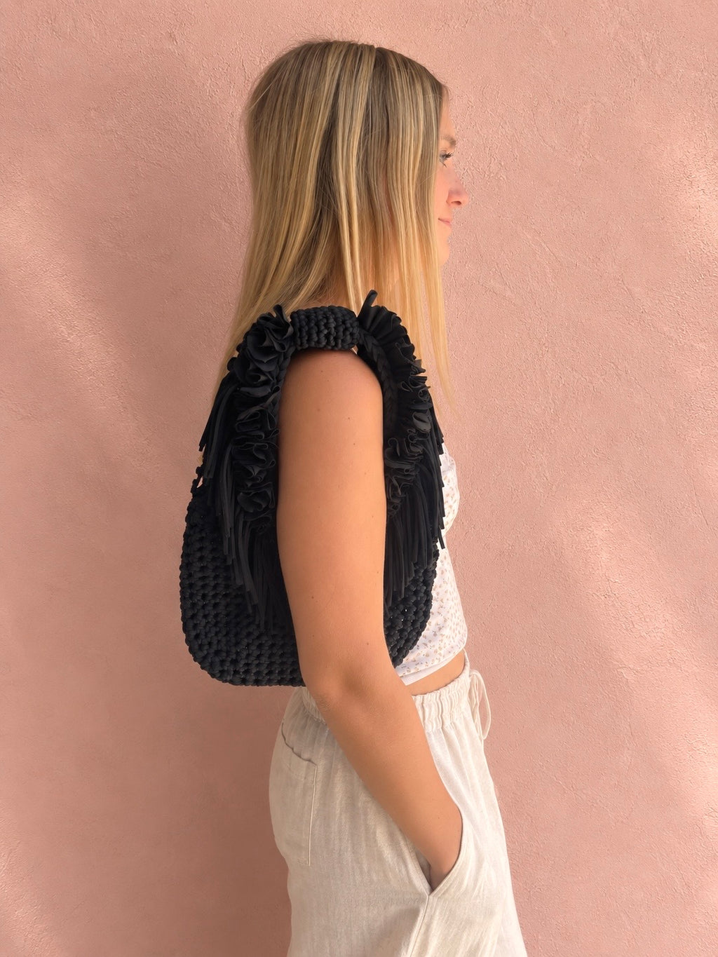 Onyx black hand-crocheted Flower Lei Mini bag with cascading floral ruffles and fringe, featuring a braided handle and sculptural mini silhouette.