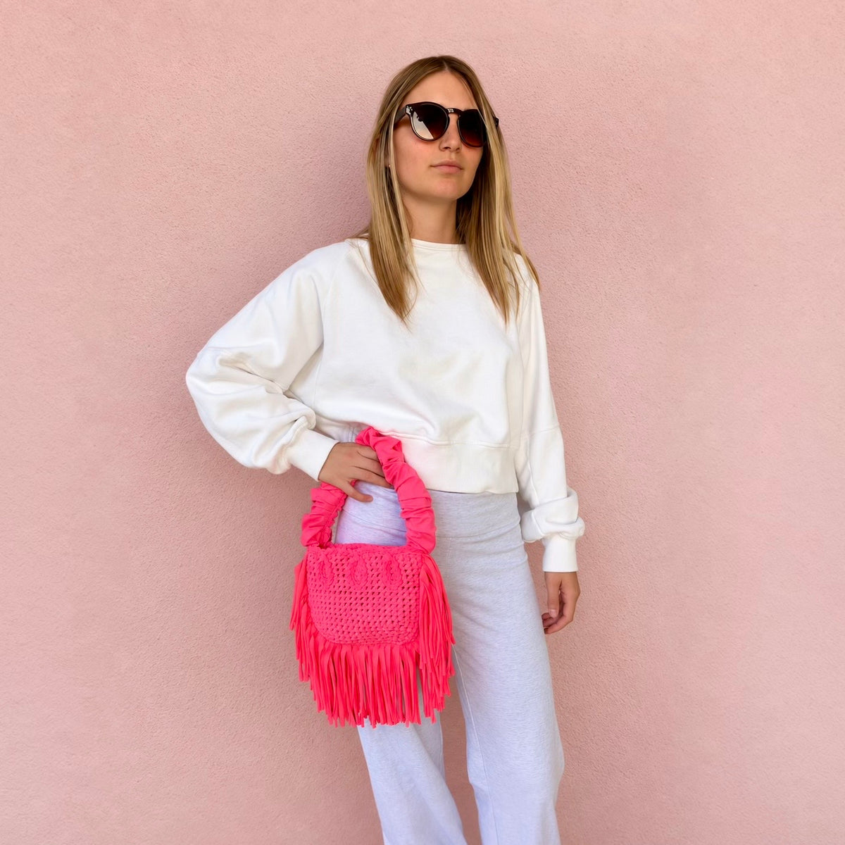 Hibiscus coral handmade crochet Cha Cha Mini bag featuring a crescent-shaped body, braided loop detailing, ruched scrunchie handle and flowing fringe. 
