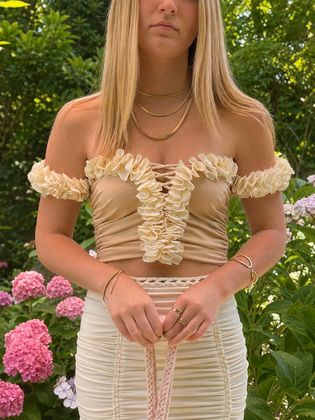 Magnolia cream floral off-the-shoulder crop top with flower lei trim and clay tan bodice with hand-crocheted lace-up center detail. Matching set includes the cream mini pencil skirt. 