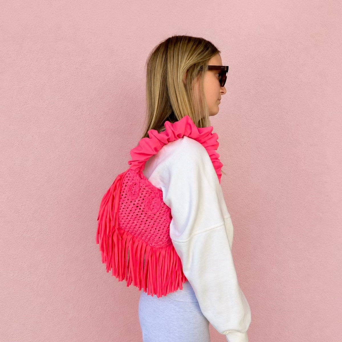 Hibiscus coral handmade crochet Cha Cha Mini bag featuring a crescent-shaped body, braided loop detailing, ruched scrunchie handle and flowing fringe. 