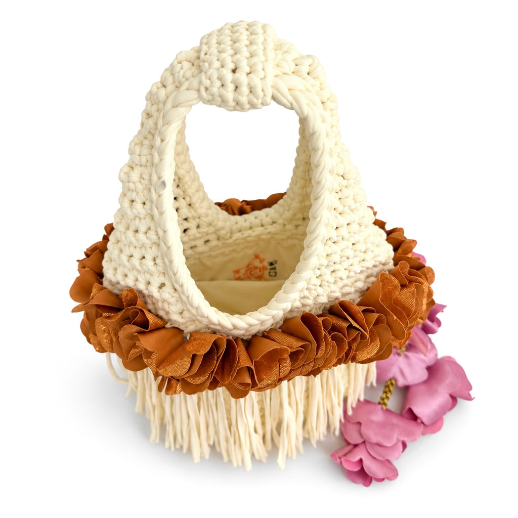 Handmade magnolia cream crochet whimsy mini bag with cascading fringe, metallic pink and copper petal bell trim and a braided handle. 